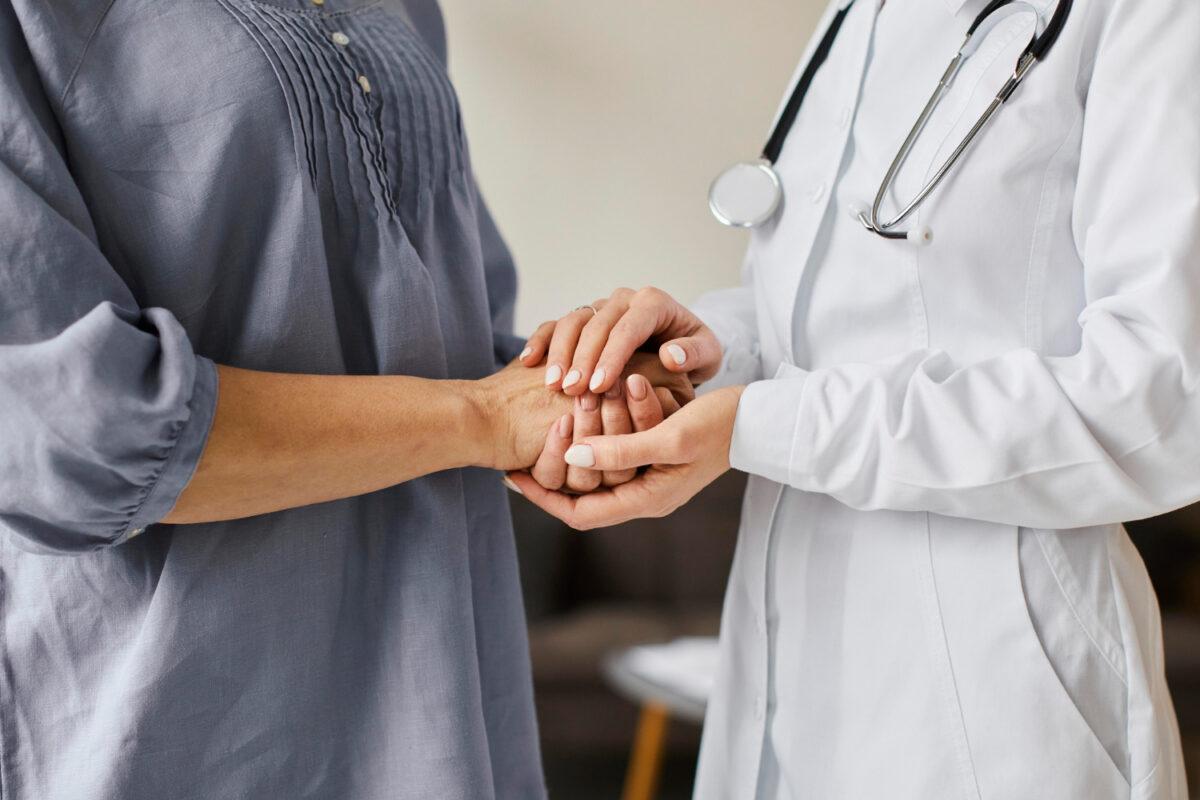 deux personnes dont une personne soignante qui tient les mains de la patiente