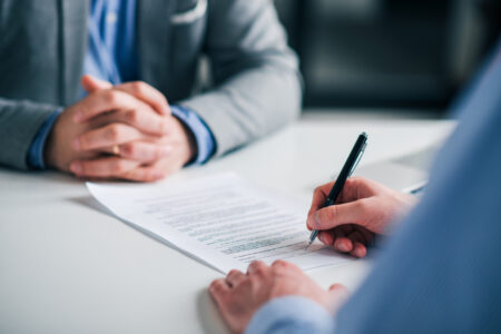 2 personnes autour d'une table qui signe un contrat; on ne voit que les mains des deux personnes. Le contrat est sur la table, une personne est en train de la signer
