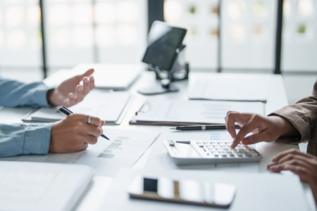 2 personnes en réunion qui échange sur des documents sur la table. On ne voit que les mains des 2 personnes