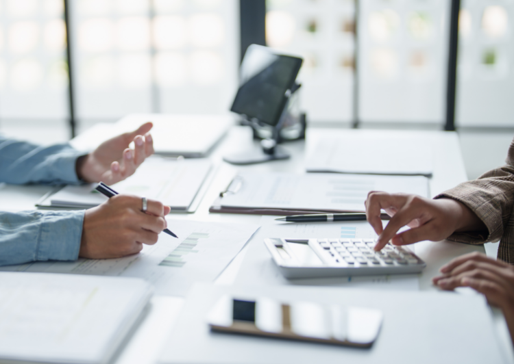 2 personnes en réunion qui échange sur des documents sur la table. On ne voit que les mains des 2 personnes