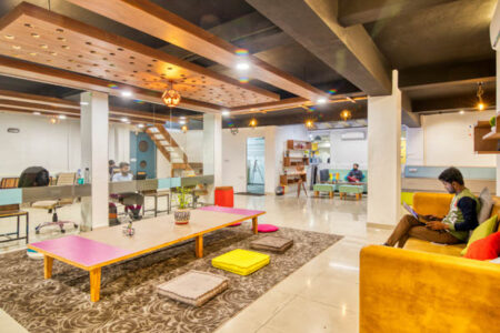 Visuel d'un open space d'une start up, longue table au milieu et une personne assise dans le canapé